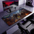 Une configuration de jeu moderne et minimaliste comprend un moniteur, un clavier et une souris sur un grand tapis de souris sur le thème de Fortnite présentant des personnages de Fortnite en costumes d'Halloween, complétés par une chaise noire élégante et une tour PC élégante.